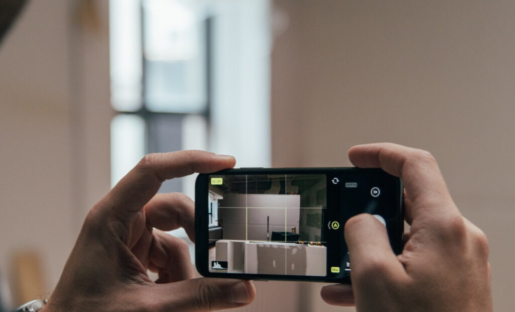 Mani che impugnano una macchina fotografica per scattare una foto a una cucina moderna bianca. Dettaglio di fotografia d’interni.